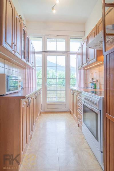 A kitchen with wooden furniture and appliances, light streaming through a large window.