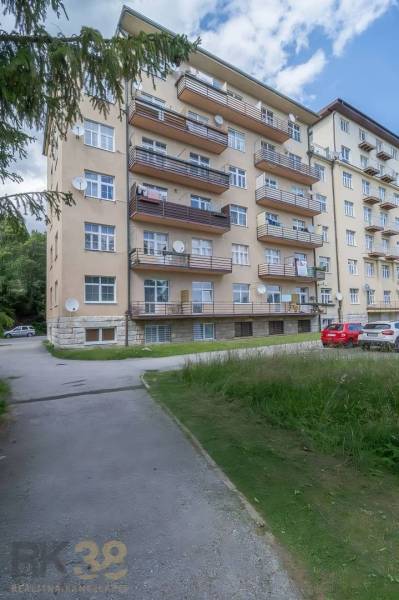 An apartment building in the High Tatras with balconies and a parking lot in front of the building.