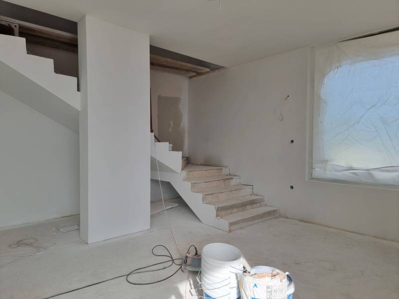The staircase in the Villa during renovation, next to a large window with a covered view.