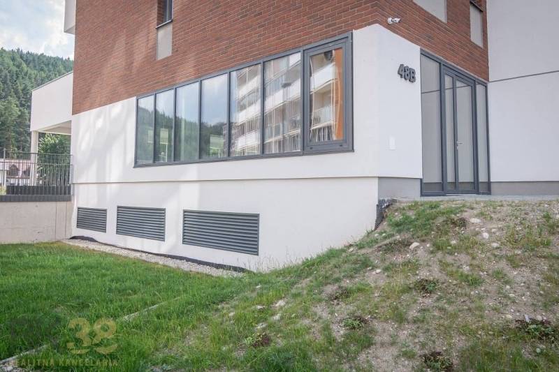 The facade of commercial spaces in the town of Svit with large windows and a green lawn.