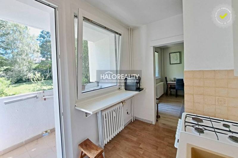 A kitchen in a 3-room apartment with a view of the balcony and surrounding greenery.