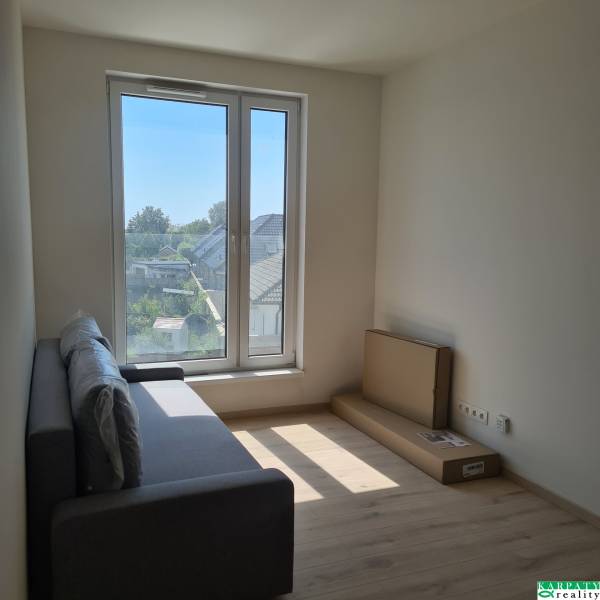 Studio apartment with a sofa, large window, and a view of the houses.