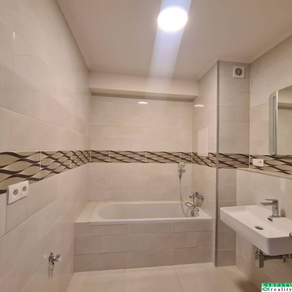 Bathroom in a studio apartment with a bathtub and a sink, ceramic tiles with a design strip.