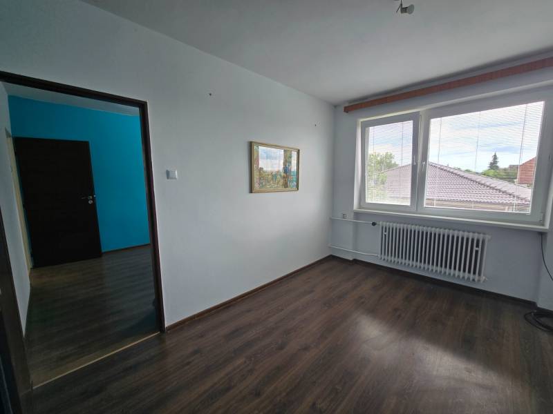 Empty room with laminate flooring in a family house, with a large window and a radiator.