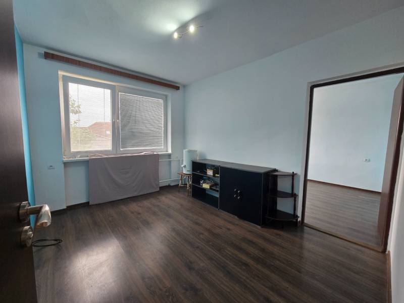 A room in a family house with a window, dark floor, light walls, furniture by the wall.