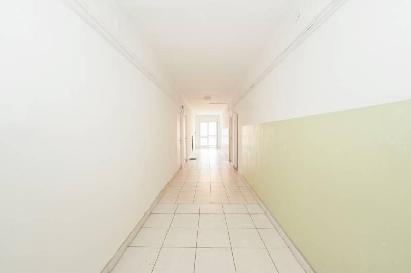 A bright hallway with white walls in an office with tiles and doors.