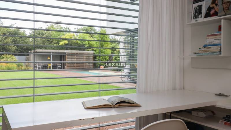 Interior of a family house with a view of the garden and pool through horizontal blinds.