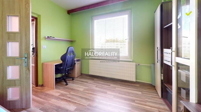 Room in a 2-room apartment with a desk, chair, green wall, and window.