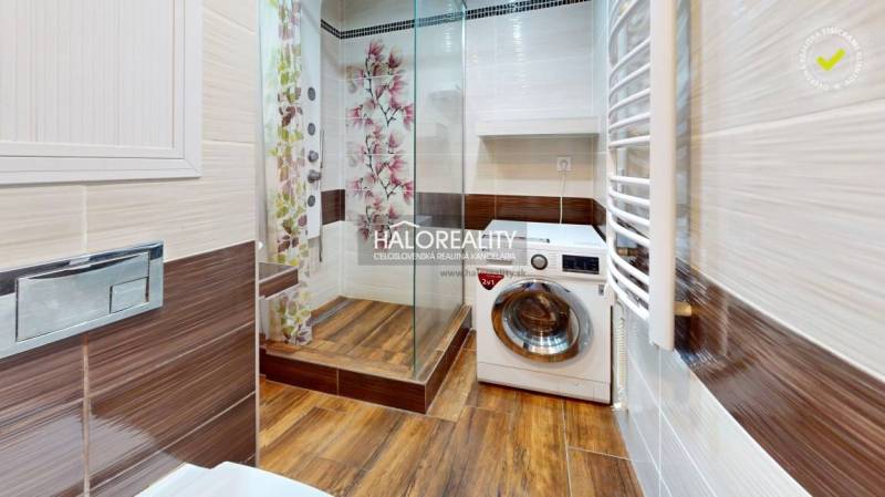 A bathroom in a 2-room apartment with a shower, washing machine, and wooden paneling.