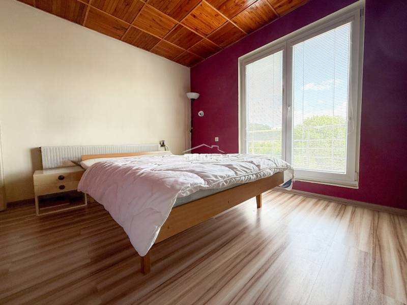 Bright bedroom in a family house with a wooden ceiling and a large window.