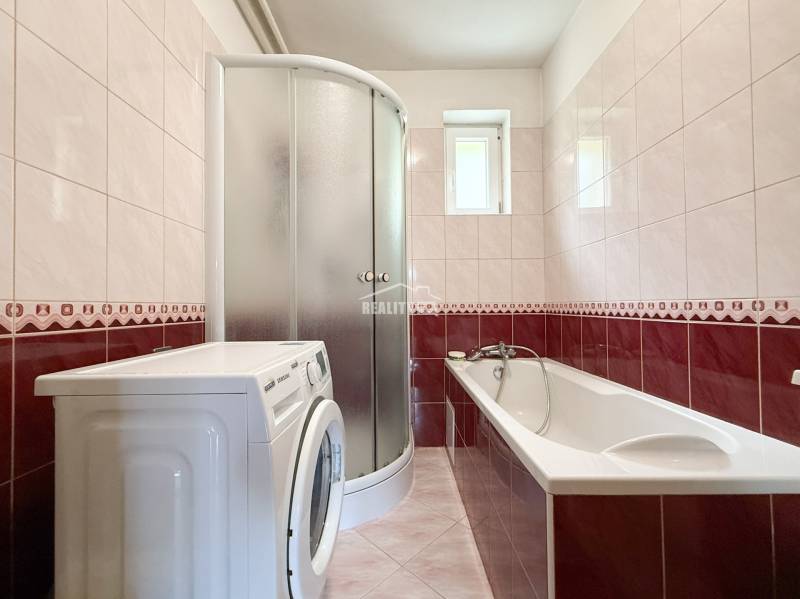 A bathroom with a bathtub, shower, and washing machine in a family house.