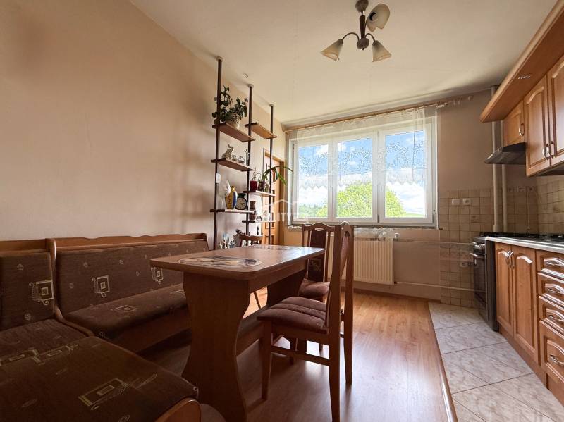A family house with a kitchen containing wooden furniture, a dining table, and a shelf with decorations.