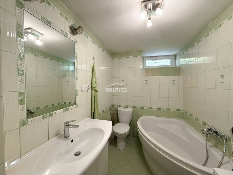 A bathroom in a family house with a bathtub, a sink, and green tiles.