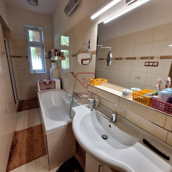 Bathroom with a bathtub and a mirror in a family house, equipped with shelves and a sink.