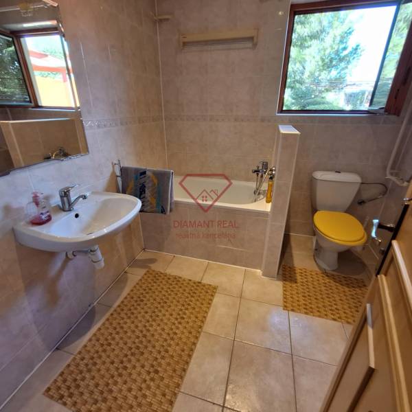 A bathroom in a family house with a bright window, a bathtub, and a sink.
