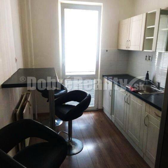 A kitchen in a 2-room apartment with a bar counter, two chairs, and white cabinets.