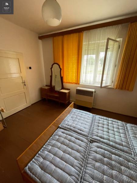 Bedroom in a family house with a window, a mirror, and a bed with a quilted mattress.