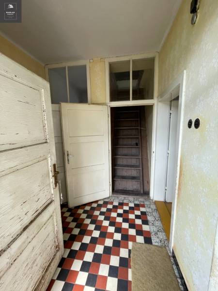 Entrance hallway in a family house with a checkered floor and wooden stairs.