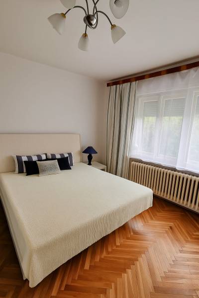 Bright bedroom in a family house with a bed, lamp, and wooden floor.