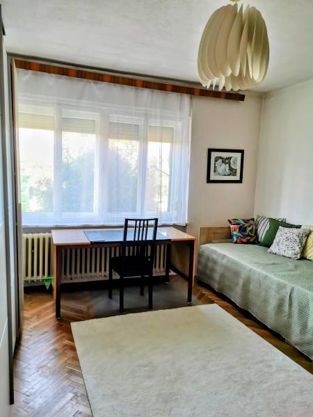A room in a family house with a desk, bed, carpet, and decorative lighting.