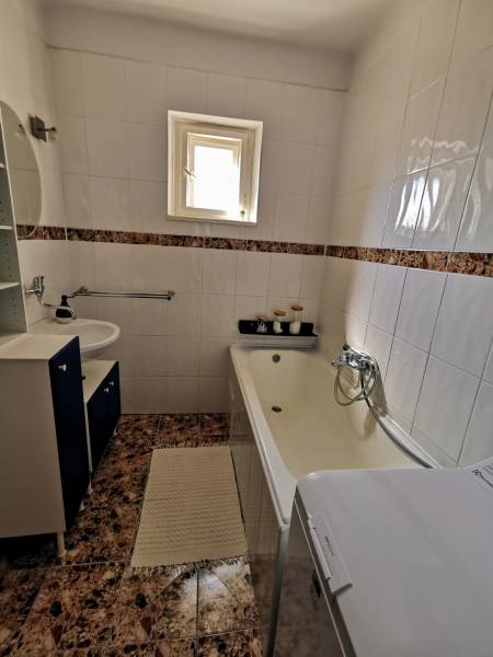 A bathroom in a family house with a built-in bathtub and sink, tiled with light tiles.