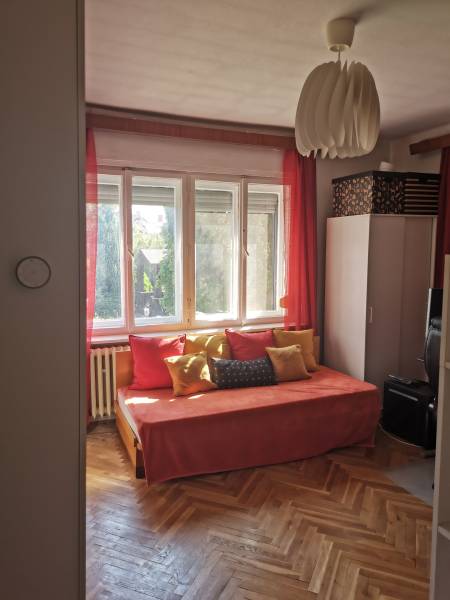 A sunny room in a family house with an orange couch, cushions, and wooden flooring.