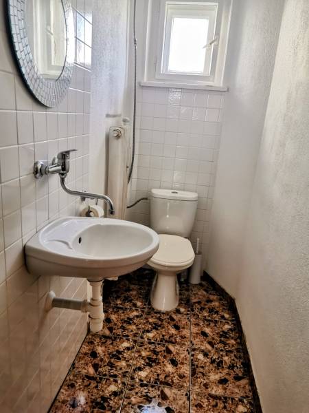 A bathroom in a family house with a sink, toilet, and window, white tiles on the walls.