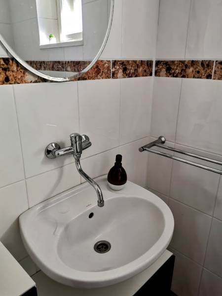 A sink in a family house with a round mirror and tiles with a brown pattern.