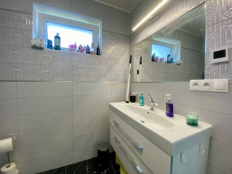 A bathroom in a family house with a sink, a mirror, and a lot of cosmetics.