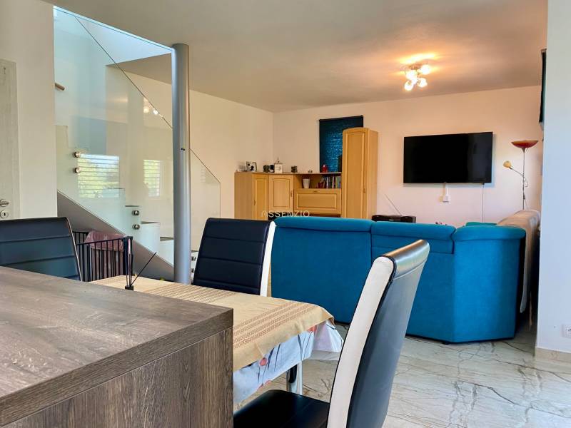 Living room in a family house with a blue sofa, dining table, and a TV on the wall.