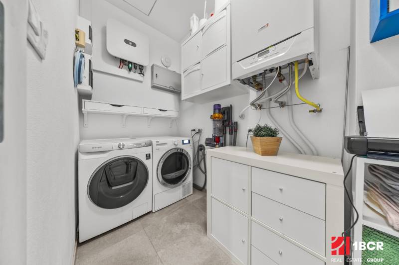 Laundry room in a family house with a washing machine, dryer, storage cabinets, and a boiler.
