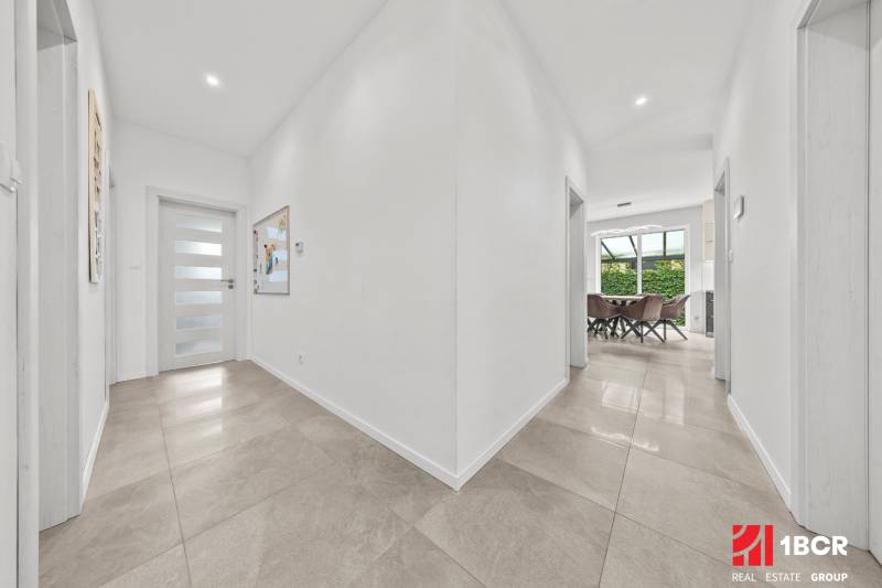 A hallway of a family house with tiles and an entrance to the dining room with a glass wall.