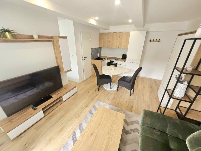 Living area with a kitchenette, wooden floors, dining table, and TV unit.