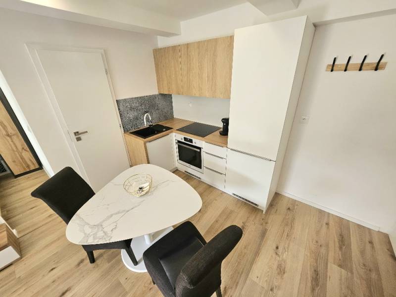 A kitchen in a studio apartment with a wooden floor, a dining table, and white cabinets.