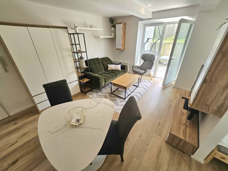 Living room in a studio apartment with a green sofa, dining table, and an armchair by the balcony.