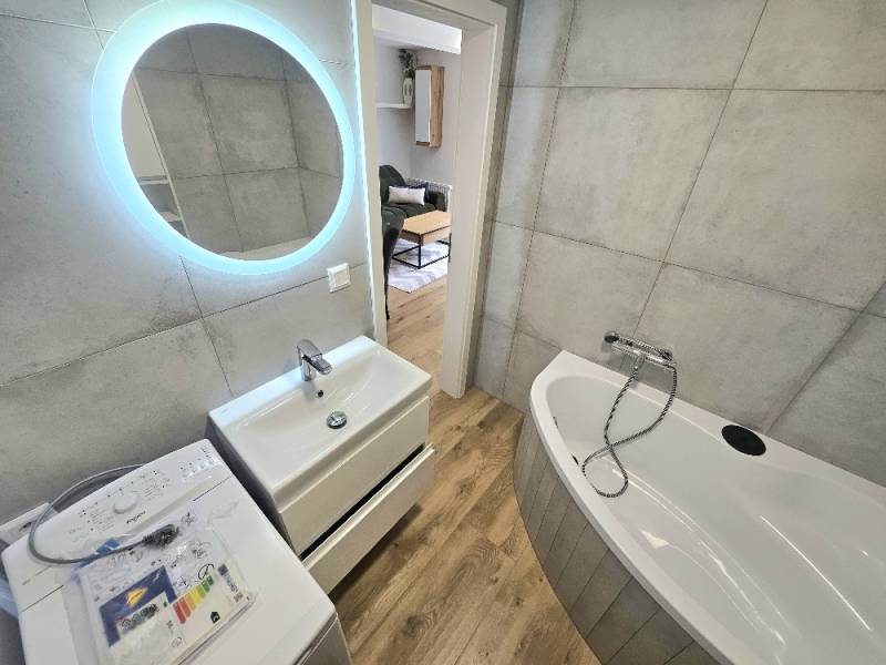 Bathroom with a bathtub, sink, washing machine, and LED lighting in a studio apartment.