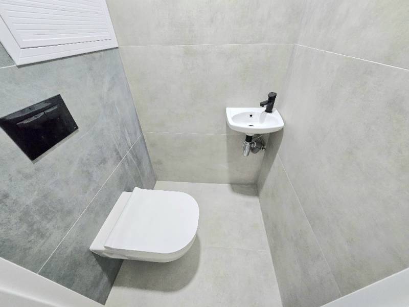 A bathroom in a 3-room apartment with a toilet and a sink, tiled with gray tiles.