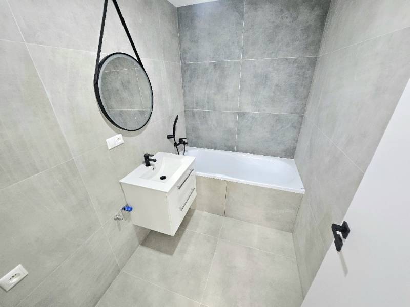 A bathroom in a 3-room apartment with a bathtub, a sink, and a mirror on the wall.