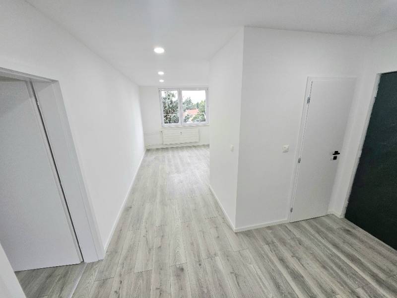 A hallway in a 3-room apartment with wooden flooring and white walls.