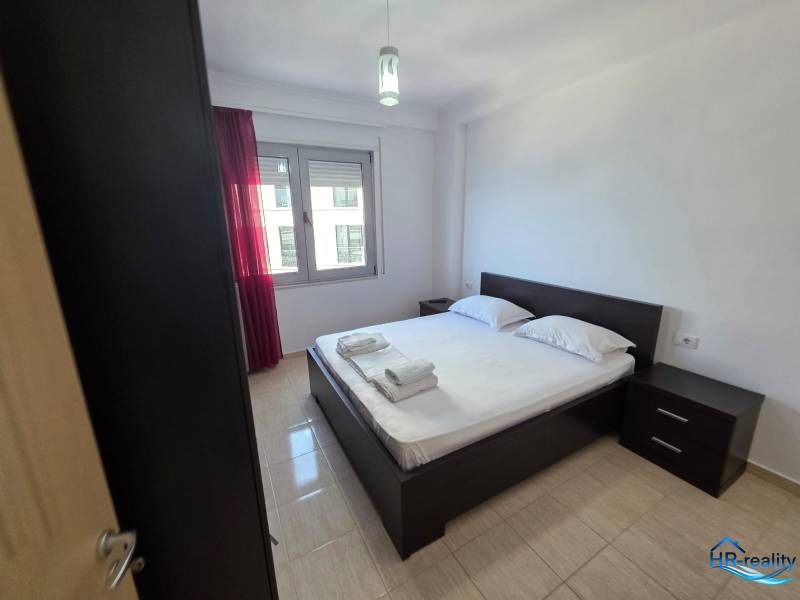 A bedroom in a holiday apartment with a double bed, nightstands, and a window with red curtains.