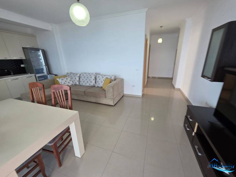 A bright living room with a kitchenette, a sofa, and a dining table in a holiday apartment.