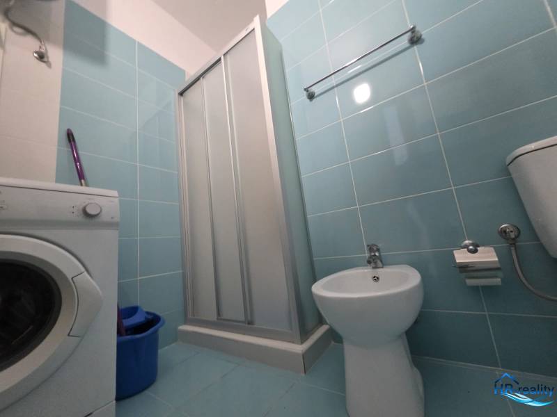 A bathroom in a holiday apartment with a washing machine, shower, and bidet.