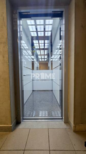 Illuminated interior of an elevator in a 3-room apartment with glass walls and tiled floor.