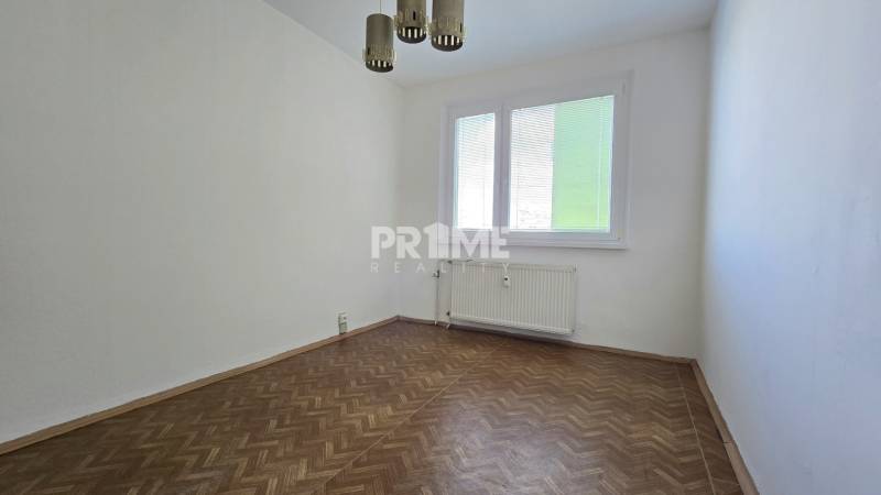 An empty room with a parquet floor, a radiator, and a window in a 3-room apartment.