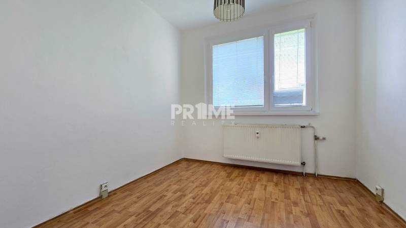 An empty room with a wooden floor and a radiator in a three-room apartment.