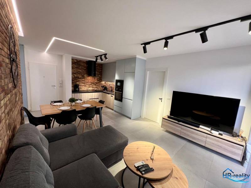 The living room of the holiday apartment is equipped with a kitchen, a dining table, and a comfortable sofa.