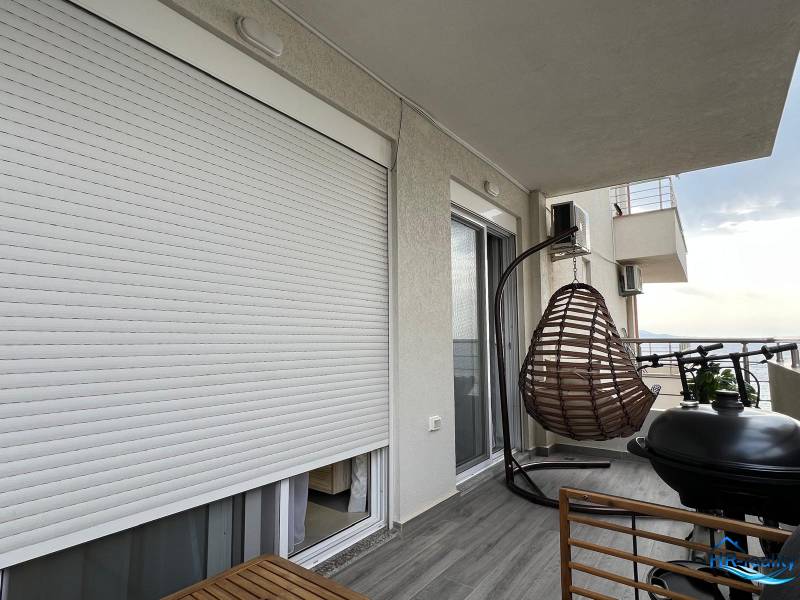 Balcony with wall-mounted blinds, hanging basket, grill, and view, recreational apartment Sarandë.