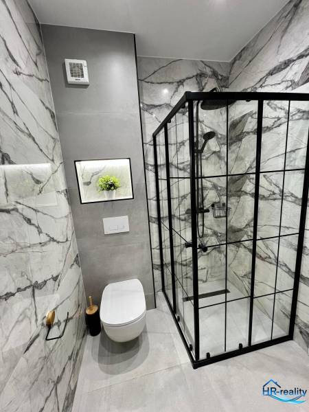 Bathroom of a holiday apartment with a toilet, shower, and marble tiles.