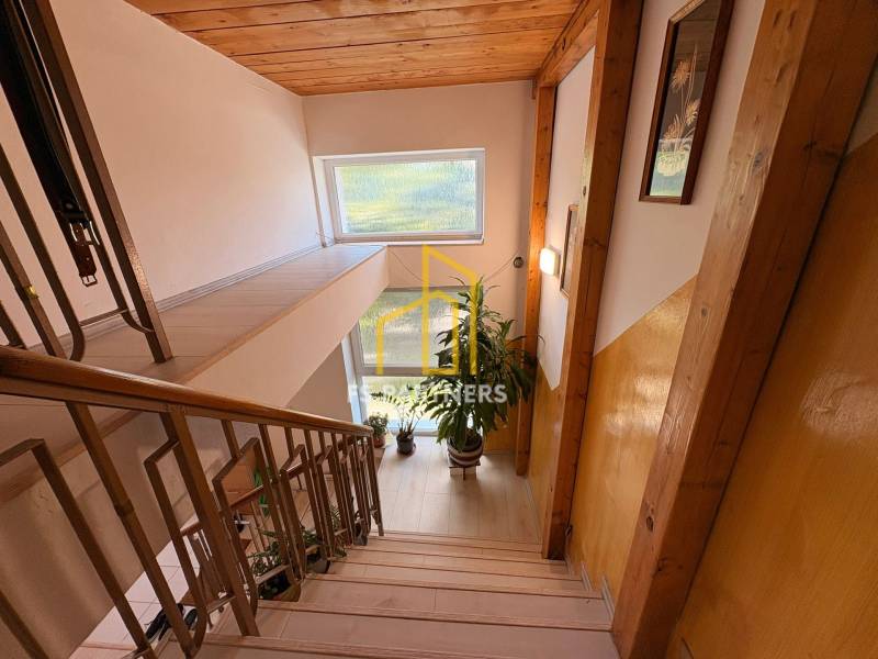 A hallway with a staircase, wooden paneling, and flowers in a family house.