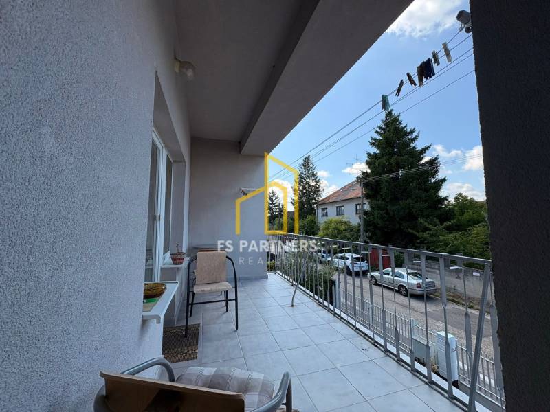 A balcony of a family house in Komárno, overlooking a street with parked cars and trees.